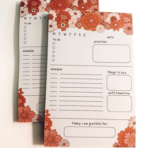 May include: Two white notepad pages with a floral border in shades of orange and pink. The pages are divided into sections for daily tasks, schedules, priorities, things to buy, and a gratitude section. The text on the pages includes "to do", "schedule", "date", "priorities", "things to buy", "until tomorrow", and "today, i am grateful for".