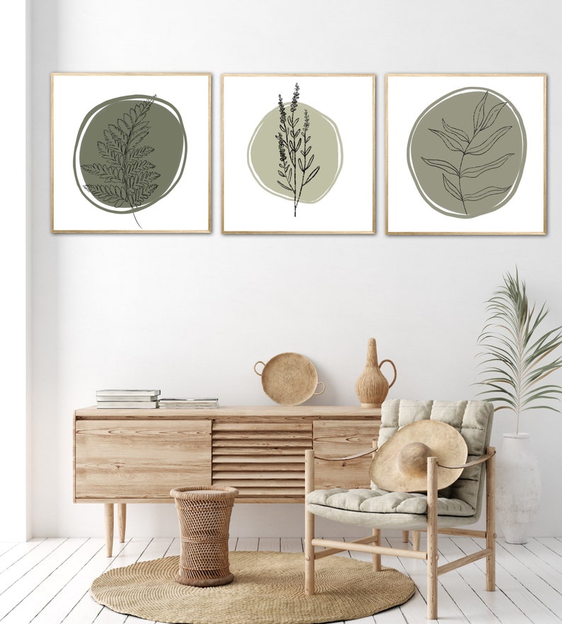 K&ouml;nnte beinhalten: Drei gerahmte Drucke mit minimalistischen Linienzeichnungen verschiedener Pflanzen auf hellgr&uuml;nem Hintergrund. Die Drucke h&auml;ngen an einer wei&szlig;en Wand &uuml;ber einer Kommode aus Holz mit einem geflochtenen Korb und einem Stuhl mit einem Strohhut.