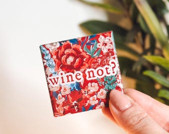 May include: A red, white, and blue floral patterned square magnet with the text "wine not?" in white letters.