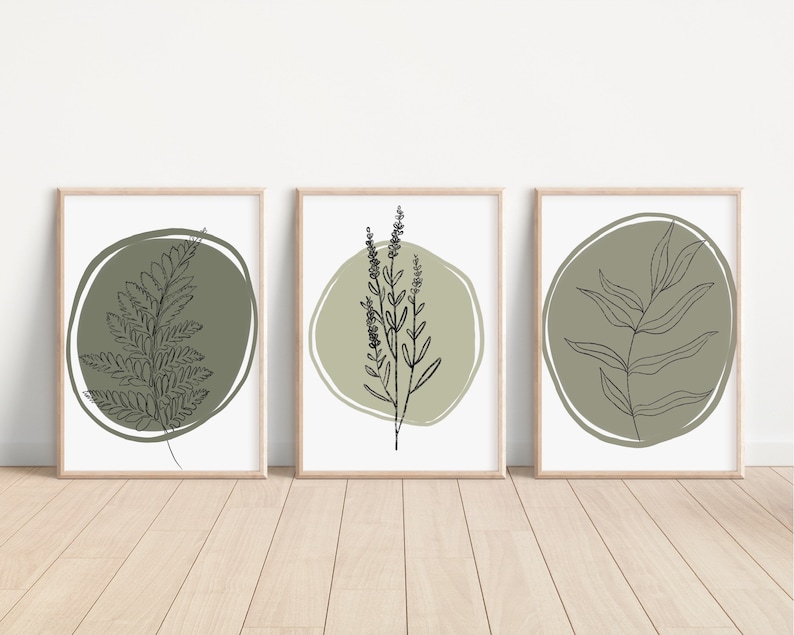 K&ouml;nnte beinhalten: Set aus drei minimalistischen Kunstdrucken mit Strichzeichnungen verschiedener Pflanzen in gr&uuml;nen Kreisen auf wei&szlig;em Hintergrund. Die Drucke sind in naturfarbenen Holzrahmen gerahmt.