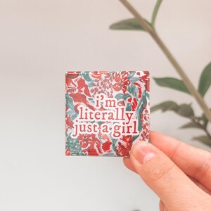 K&ouml;nnte beinhalten: Ein quadratischer Magnet mit einem floralen Muster in Rot-, Gr&uuml;n- und Wei&szlig;t&ouml;nen. Der Magnet tr&auml;gt den Text "i'm literally just a girl" in wei&szlig;en Buchstaben.