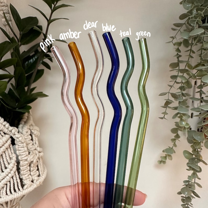 Pu&ograve; includere: Set di sette cannucce da bere in vetro di vari colori, tra cui rosa, ambra, trasparente, blu, verde acqua e verde. Le cannucce sono tutte ondulate e sono tenute in una mano.