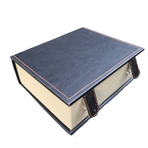 May include: A black leather box with a beige interior and two black leather straps. The box has a stitched orange border.