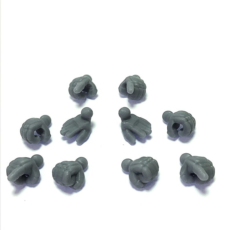 Puede incluir: Colecci&oacute;n de diez peque&ntilde;as manos de pl&aacute;stico gris en varias poses, incluyendo pu&ntilde;os y gestos de se&ntilde;alar. Las manos est&aacute;n espaciadas sobre un fondo blanco, sugiriendo un componente de juguete o modelo.