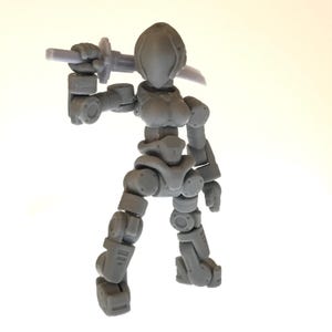 May include: A gray articulated action figure of a female warrior, holding a sword. The figure has a detailed, mechanical design with multiple points of articulation. The figure is posed in a dynamic stance, as if ready for battle.