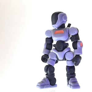 Puede incluir: Figura de acción de robot articulado en tonos lavanda, negro y naranja. La figura tiene un casco redondeado, articulaciones y un detalle naranja rectangular en el pecho. El robot está sobre un fondo blanco.