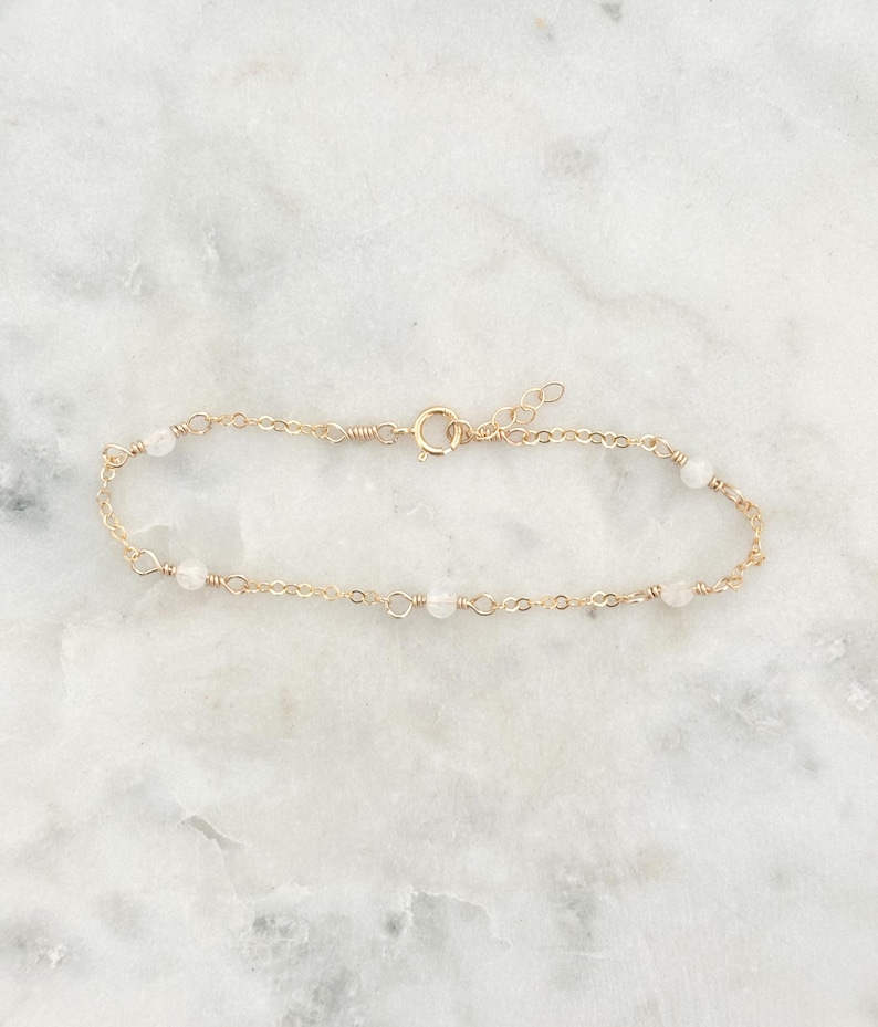 May include: A delicate gold chain bracelet with small white beads. The bracelet has a lobster clasp closure.