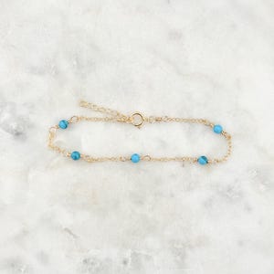 May include: A delicate gold chain bracelet with small turquoise beads. The bracelet has a lobster clasp closure.
