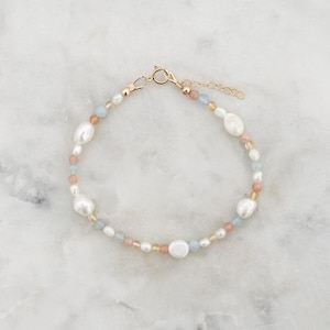 May include: A delicate bracelet featuring a mix of white baroque pearls, small blue and peach-colored beads, and gold-toned accents. The bracelet has a gold clasp and an adjustable chain for a comfortable fit. This jewelry piece is perfect for adding a touch of elegance.