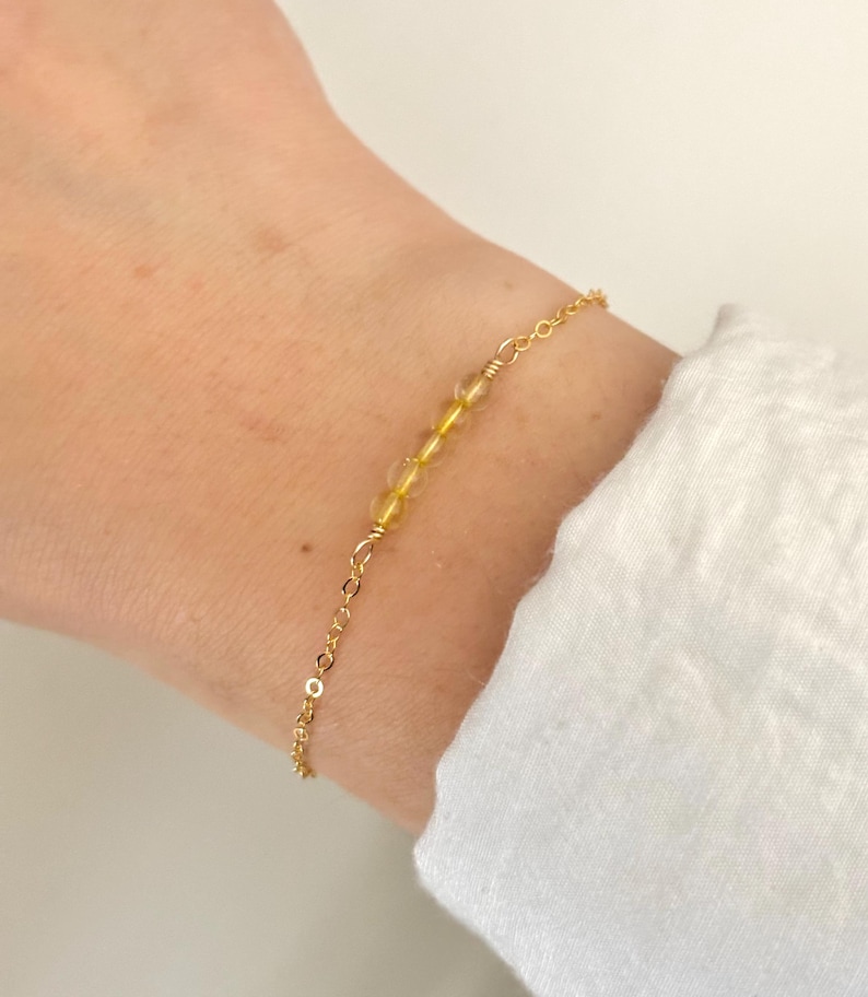 May include: A gold chain bracelet with small, clear yellow beads.