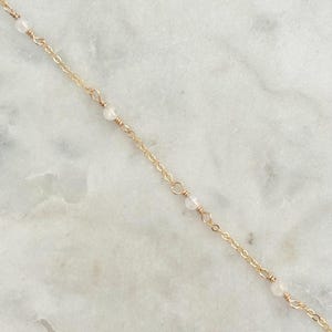 May include: A delicate gold chain necklace with small white beads.