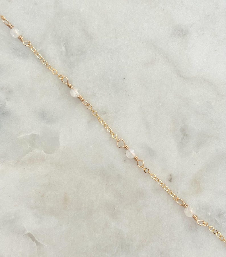 May include: A delicate gold chain necklace with small white beads.