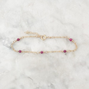 May include: A delicate gold chain bracelet with small, deep pink beads.