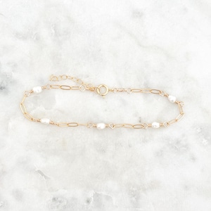 May include: A delicate gold chain bracelet with small white pearls spaced evenly along the chain.