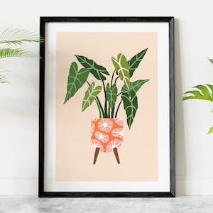 Könnte beinhalten: Ein gerahmter Druck einer stilisierten Illustration einer grünen Pflanze in einem rosafarbenen und weißen gemusterten Topf mit Holzbeinen auf einem pfirsichfarbenen Hintergrund.