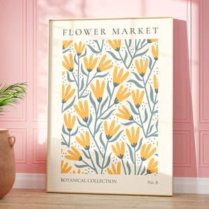 Può includere: Una stampa incorniciata con un motivo floreale. La stampa presenta fiori gialli con steli e foglie blu su uno sfondo bianco. Il testo "FLOWER MARKET" è in cima alla stampa, e "BOTANICAL COLLECTION No. 8" è in fondo.