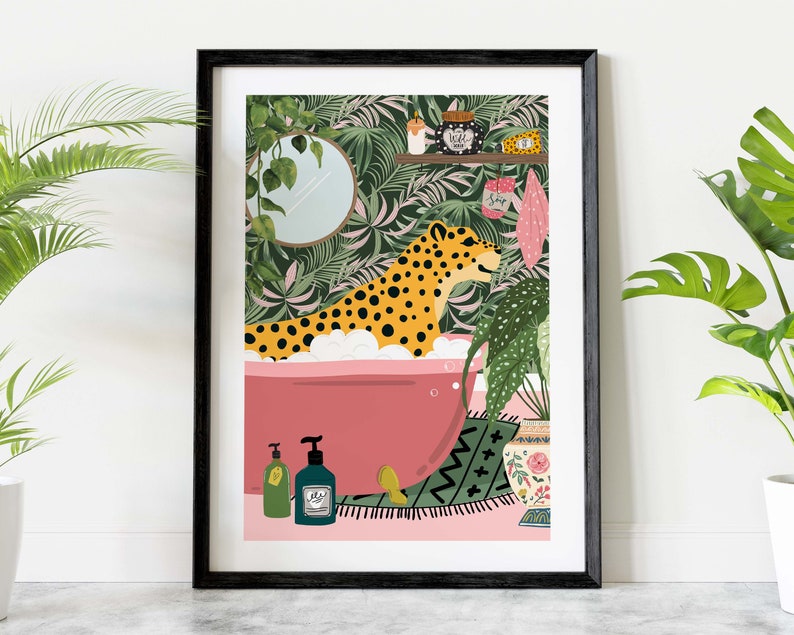 This colourful bathroom print features a leopard sitting in a pink bathtub surrounded by bottles and plants.  The background shows a tropical green wallpaper with scrubs and a candle on a shelf. A mirror with trailing ivy hang on the wall.