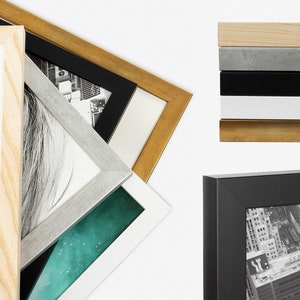 May include: A variety of picture frames in different colors and styles, including natural wood, silver, black, and gold. The frames are stacked on top of each other, with the top frame being a natural wood frame.