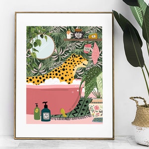 This colourful bathroom print features a cheetah sitting in a pink bathtub surrounded by bottles and plants.  The background shows a tropical green wallpaper with scrubs and a candle on a shelf. A mirror with trailing ivy hang on the wall.