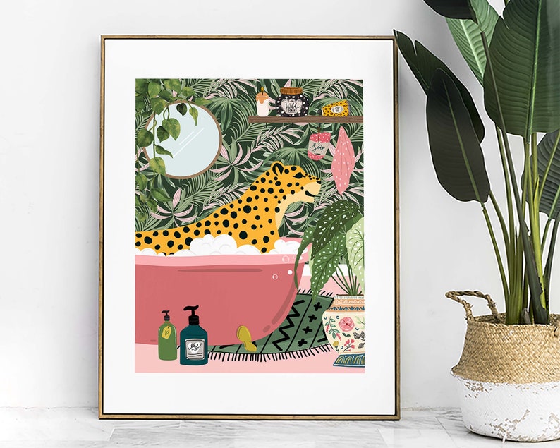 This colourful bathroom print features a cheetah sitting in a pink bathtub surrounded by bottles and plants.  The background shows a tropical green wallpaper with scrubs and a candle on a shelf. A mirror with trailing ivy hang on the wall.