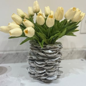 May include: A bouquet of white tulips arranged in a vase made of stacked oyster shells.