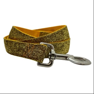 Op de afbeelding: Een gouden glitter hondenriem met een zilveren metalen sluiting. De riem heeft een heldere goudkleur met een glittertextuur. De metalen sluiting is bevestigd aan het uiteinde van de riem.