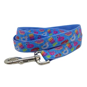 May include: A blue dog leash with a repeating pattern of pool floats, including flamingos, donuts, and popsicles. The leash has a silver metal clasp for easy attachment to a collar.
