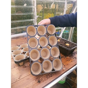 May include: Two black plastic trays with 12 biodegradable peat pots each. The pots are brown and made of compressed peat moss. The trays are used for starting seeds or seedlings.