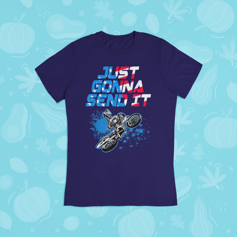 Puede incluir: Una camiseta azul marino con un gr&aacute;fico de un piloto de motocross realizando un truco. El texto "JUST GONNA SEND IT" est&aacute; impreso en rojo, blanco y azul en la camiseta.