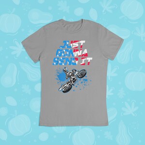 Puede incluir: Camiseta gris con un gr&aacute;fico de un piloto de motocross realizando un truco. El texto "JUST GONNA SEND IT" est&aacute; impreso en la camiseta en rojo, blanco y azul.