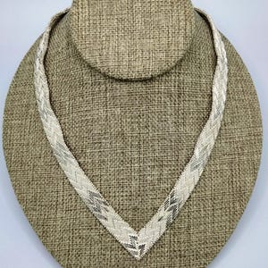 May include: A silver herringbone chain necklace on a brown fabric display stand.