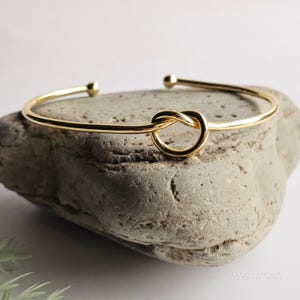 May include: A gold knot bangle bracelet. The bracelet is simple and delicate, with a knot design in the centre.
