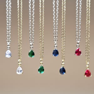 May include: A collection of delicate necklaces with teardrop-shaped pendants. The pendants are in various colors, including clear, green, blue, and red. The chains are either silver or gold-colored, creating a contrast with the gemstones.
