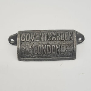 May include: A silver metal drawer pull with the words "Covent Garden London" embossed on it.