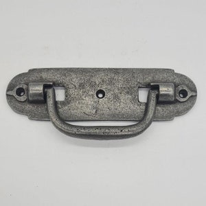 May include: A silver-toned metal drawer pull with a rectangular base and a curved handle. The pull has a distressed finish and a slightly ornate design.