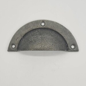May include: A silver metal cup pull handle with a rounded shape and three holes.