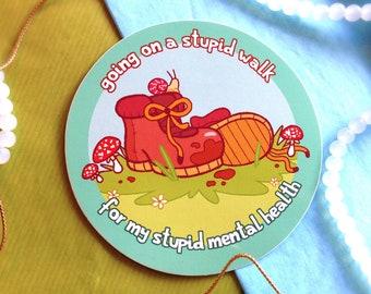 May include: A round sticker with a light blue background and a cartoon illustration of a red hiking boot with a snail on top. The text on the sticker reads "going on a stupid walk for my stupid mental health".