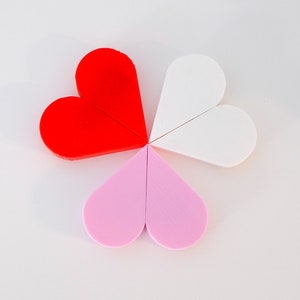 May include: Four heart-shaped pieces of felt in red, white, and pink. The pieces are arranged in a circle, with the red piece at the top.