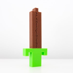 May include: A brown plastic sword with a green plastic handle. The sword has the text "ALKDesignStudio" printed on the side.