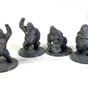 Op de afbeelding: Vier grijze, plastic miniatuur gorilla-figuurtjes. De gorilla's staan in verschillende poses, waaronder staand, zittend en hurkend. De figuurtjes staan op kleine, ronde bases.