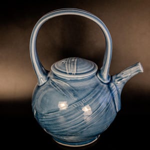 May include: A blue ceramic teapot with a rounded body and a curved handle. The teapot has a lid with a small spout and a decorative design.