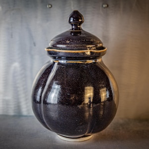 May include: A dark blue ceramic jar with a lid and a fluted body. The jar has a glossy finish and a subtle sheen.
