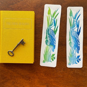 May include: Two blue and green bookmarks with a bird design. The bookmarks are on a wooden surface. The text "THE FOUR SEASONS" is on a yellow book.