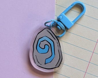 May include: A light blue keychain with a clear acrylic charm featuring a gray swirl design.