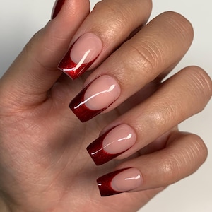 May include: Close-up of a hand with red and nude nail polish. The nails are long and square-shaped with a red half-moon design at the base.