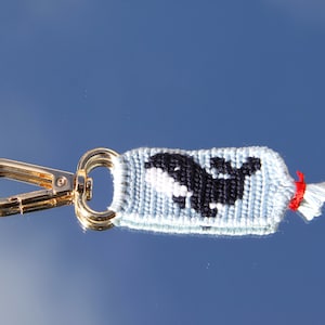 May include: A blue and black woven keyring with a whale design and a gold metal clasp.