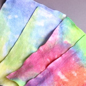 May include: Four pieces of tie-dye fabric in shades of blue, green, pink, and purple. The fabric is folded and layered, creating a colorful and abstract pattern.