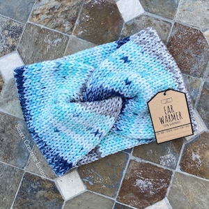 May include: A blue and white knitted ear warmer with a brown tag that reads "Ear Warmer 100% Handmade". The tag also includes the text "100% Yarn - Top Quality - Chic & Unique".