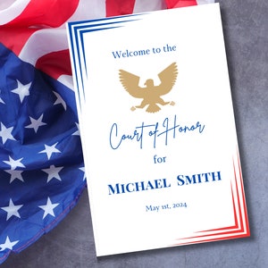 Peut inclure: Une carte blanche avec des bordures bleues et rouges. La carte indique "Bienvenue au tribunal d'honneur pour MICHAEL SMITH 1er mai 2024". Un aigle doré est au-dessus du texte "Cour d'honneur".