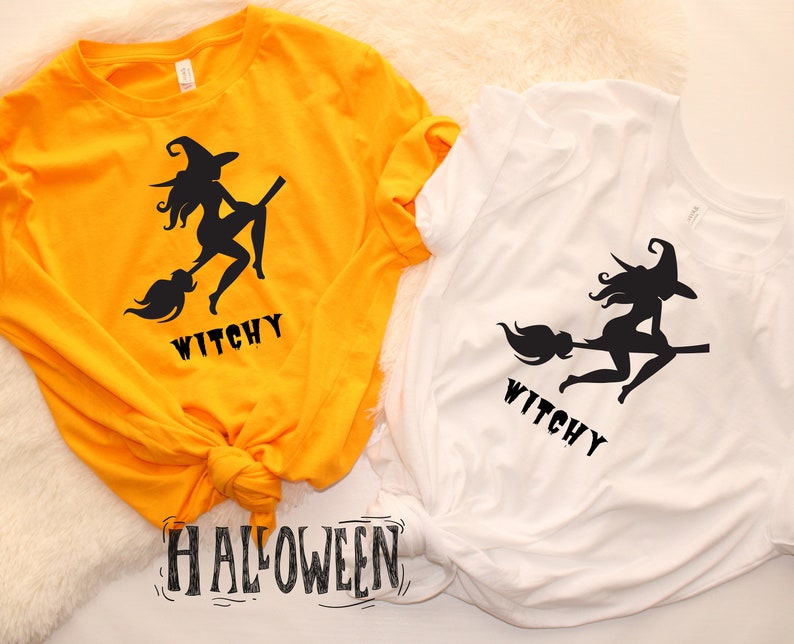 May include: Two t-shirts featuring a witch silhouette design with the word "Witchy" printed on them. The shirts are yellow and white. The word "Halloween" is written in black on a white background.